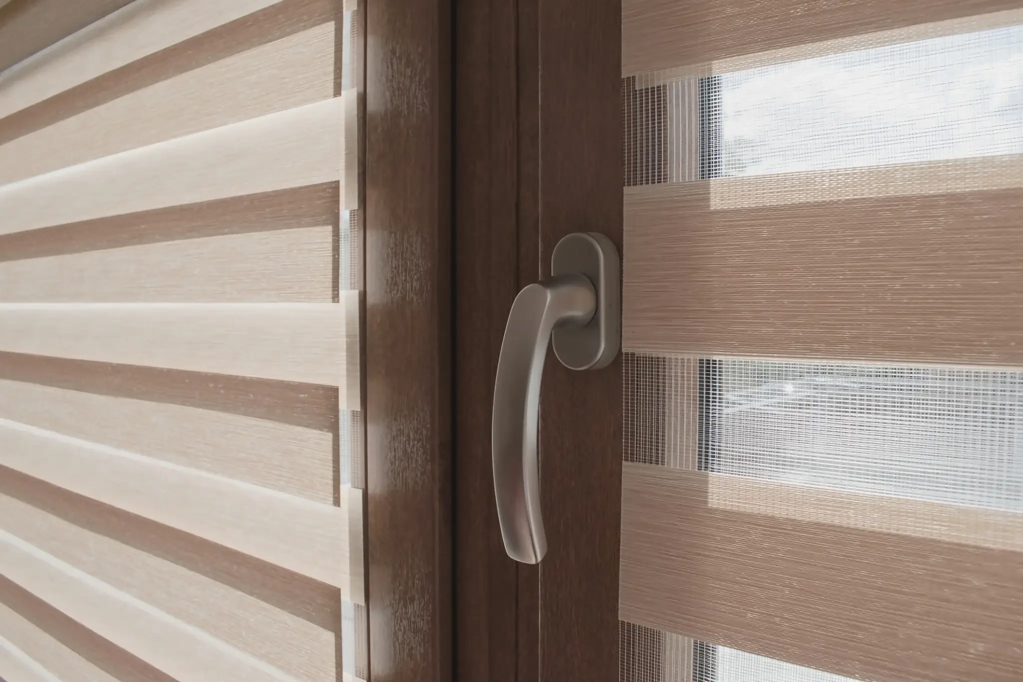 

Rolety Dzień Noc w beżowych odcieniach zamontowane na drewnianym oknie — zbliżenie na tkaninę w pasy i klamkę okienną.
